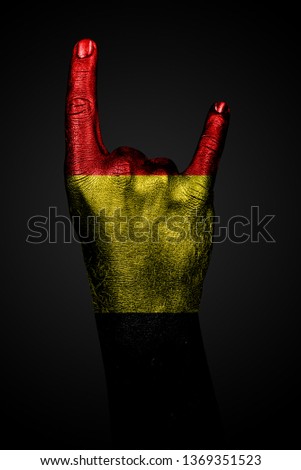 A hand with the painted flag of Belgium shows an OK sign on a dark background. Vertical frame