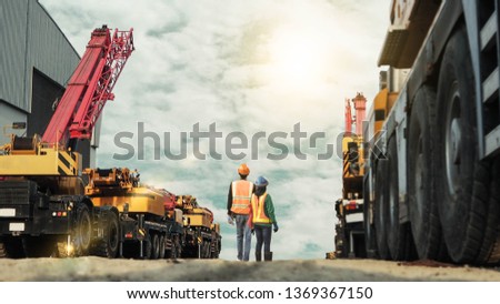 Blurred construction engineer and women worker wearing PPE safety to checking mobile crane in construction site, Royalty-Free Stock Photo #1369367150