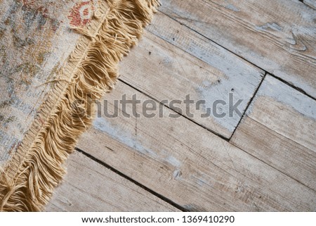 Fringe of the carpet and texture of the wooden floor.