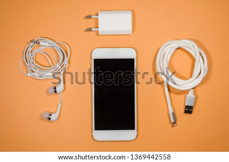 a phone with white usb cable, block and headphones on orange background. Keep the battery charged and listen to music on your device anyway you go. Tehnology connect close up.