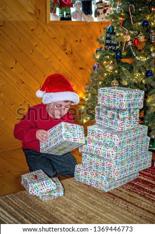 small boy in red santa hat, checks out wrapped packages under the Christmas tree