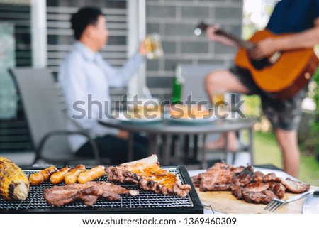 Group of friends Two young man enjoying grilled meat and play guitar with raise a glass of beer to celebrate the holiday festival happy drinking beer outdoors and enjoyment at home.