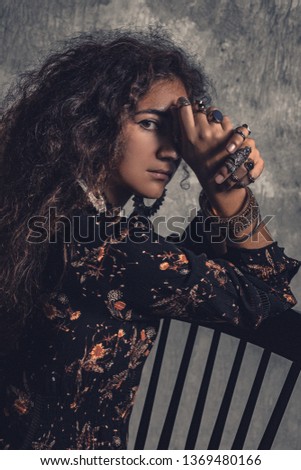 young beautiful woman in elegant dress with boho accessories sitting on chair 