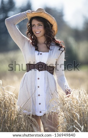 Beautiful young lady in the field with a cowboy hat