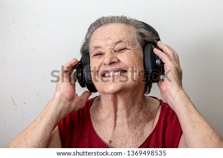 Lifestyle and people concept: Funny old lady listening music and dancing on white background. Elderly woman wearing glasses dancing to music listening on his headphones.