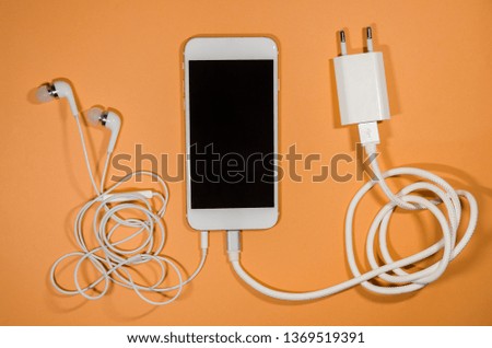 a phone with white usb cable block and headphones on orange background. Keep the battery charged and listen to music on your device anyway you go. Tehnology connect close up.