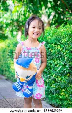 Portrait of happy asian little girl with doll standing on footpath in the park