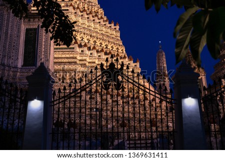 Looking through the wall fence that surrounds the Phra Prang, Wat Arun at night. On the fence there is a statue of Garuda