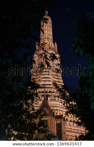 The light of Phra Prang, Wat Arun at night. There are branches in the foreground.