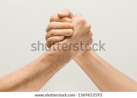 Friends greetings sign or disagreement. Two male hands competion in arm wrestling isolated on grey studio background. Concept of standoff, support, friendship, business, community, strained relations.