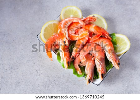 plate of boiled shrimps with lemon, on a light gray table, top view