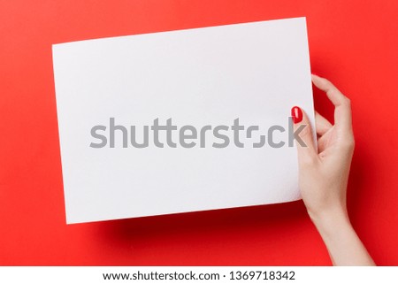 Woman hands holding a white a blank A4 paper on a red background