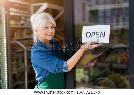 Senior woman holding open sign in organic produce shop
