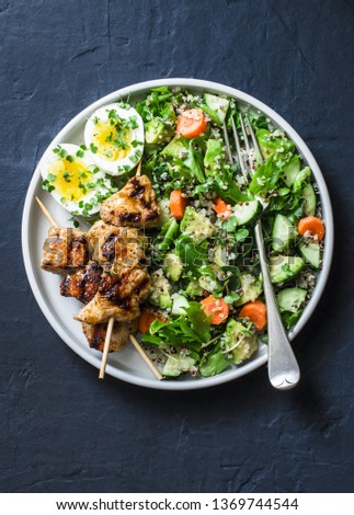 Healthy balanced lunch bowl - turkey skewers, quinoa, avocado, cucumber salad and boiled egg on dark background, top view. Mediterranean style food               