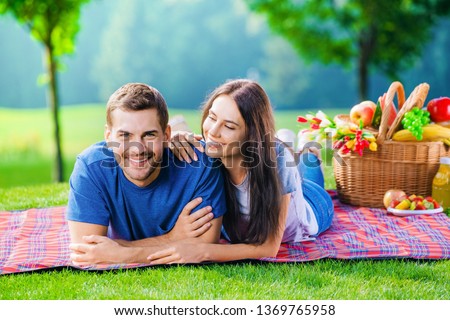 Bright photo of young happy smiling couple in love, lying together on a picnic blanket, outdoors