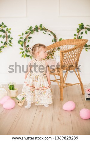 Cute little girl in a dress with a floral print in the Easter decorations in the studio. Little girl with easter eggs and flowers in a spring studio
