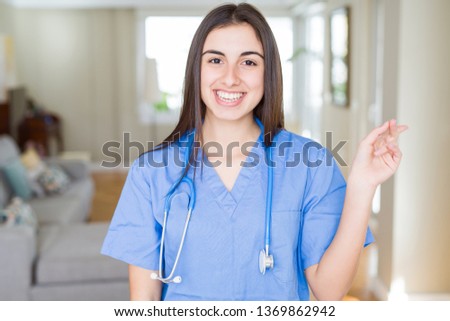 Beautiful young nurse woman wearing uniform and stethoscope at the clinic with a big smile on face, pointing with hand and finger to the side looking at the camera.