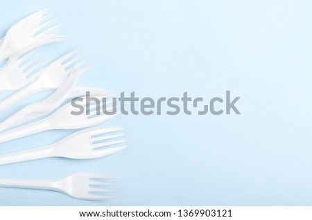 Plastic white disposable forks and knives on a blue background. Concept plastic dishes, fast food, plastic pollution. Copy space, top view, flat lay.
