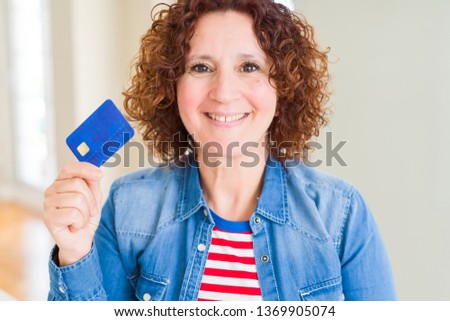 Senior woman holding credit card as payment with a happy face standing and smiling with a confident smile showing teeth
