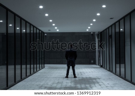 Back view of a standing man in the modern, urban surroundings. Night dramatic scene. Converging perspective.