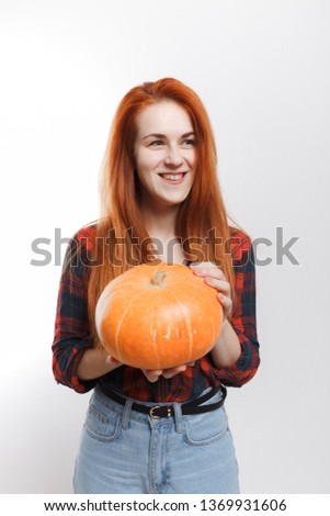 young girl farmer with red hair holding a crop from the field: juicy and fresh pumpkin. street style clothes: stylish jeans and plaid shirt. emotional portrait of a woman agronomist
