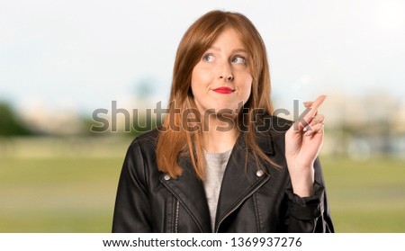 Young redhead woman with fingers crossing and wishing the best at outdoors