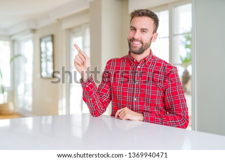 Handsome man wearing colorful shirt with a big smile on face, pointing with hand and finger to the side looking at the camera.