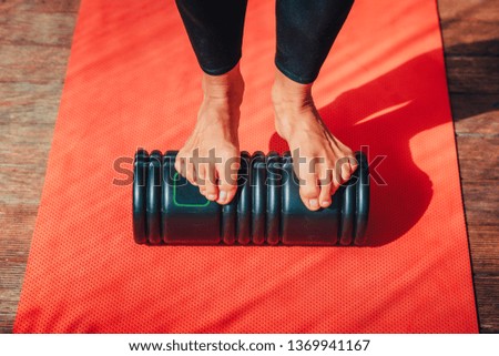 Woman's feet standing on black massage roller. Exercise concept photo, red background