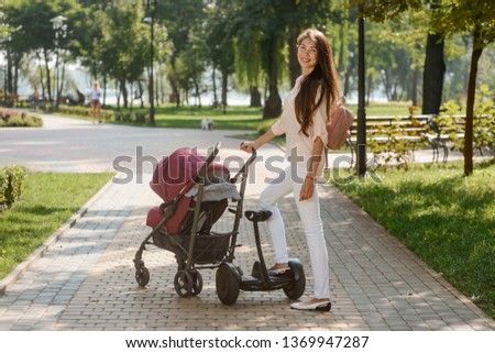 Mother walking with a pram and riding an electronic scooter in the park. Modern transport technologies, eco gadgets for urban life.