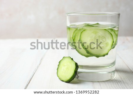 Glass cup with dietary refreshing water with cucumber on wooden table on neutral background. Concept detox drink.