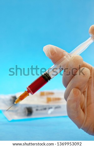 closeup of hand holding injection syringe with red fluid against blue background