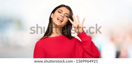 Teenager girl with red sweater happy and counting four with fingers at outdoors