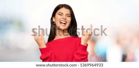 Teenager girl with red sweater making rock gesture at outdoors