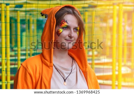 Woman in a Fox costume on the background of trampolines. The girl in the hood with ears squirrels. Face painting in the form of butterflies. Fabulous animal sweatshirt on a young woman.