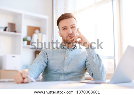 Portrait of handsome man looking at camera while sitting at workplace lit by sunlight, copy space Royalty-Free Stock Photo #1370008601