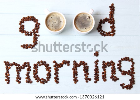 
the words "Good morning" laid out from coffee beans and a cup of coffee on a colored background top view.