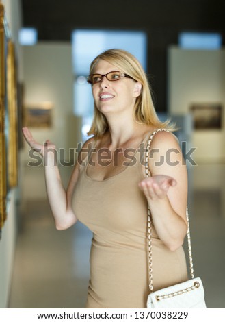 Woman wearing glasses throwing up her hands near the picture in art museum hall