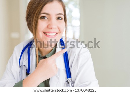 Beautiful young doctor woman wearing medical coat and stethoscope cheerful with a smile of face pointing with hand and finger up to the side with happy and natural expression on face
