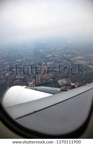 Images from the plane window while flying saw wing, engine and the city below The picture has a slightly black border or vignette.