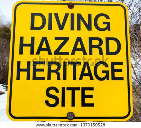 A bright yellow sign saying 'DIVING HAZARD HERITAGE SITE' is posted at a public dock.