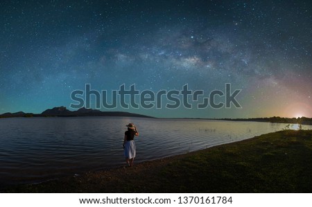 The Silhouette of an Asian woman standing alone with loneliness, sadness, disappointment from love. Outdoor lakeside on the night of the stars and the Milky Way. Long Exposure, with grain.