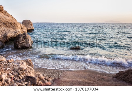 landscape picture background of a beach with sand mounds, stones cliff, blue sea with waves and sky