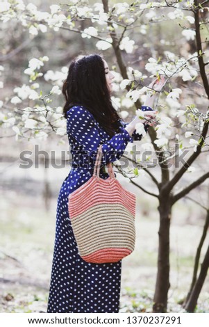 beautiful brunette woman in a blue dress and a knitted bag near magnolia blooming
