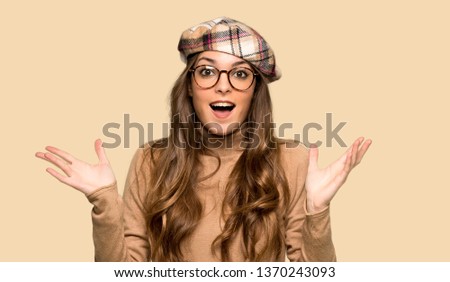 Young woman with beret with surprise and shocked facial expression over isolated yellow background