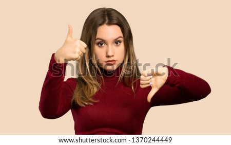Teenager girl with turtleneck making good-bad sign. Undecided between yes or not over isolated ocher background