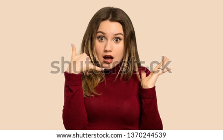 Teenager girl with turtleneck making phone gesture and doubting over isolated ocher background