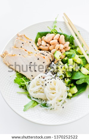 Healthy balanced food, bowl of glass noodles, beans, chicken breast, spinach, arugula and cucumber. White background, side view