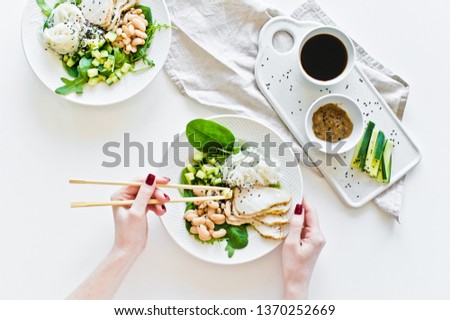 Girl holding chopsticks, Buddha bowl with glass noodles, beans, chicken breast, spinach, arugula and cucumber. White background, top view, space for text