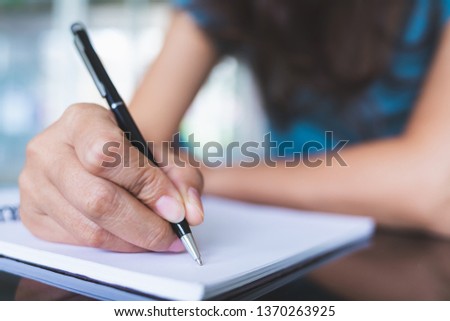 Close-up pictures of women using a black pen to write on a blank notebook on a glass table