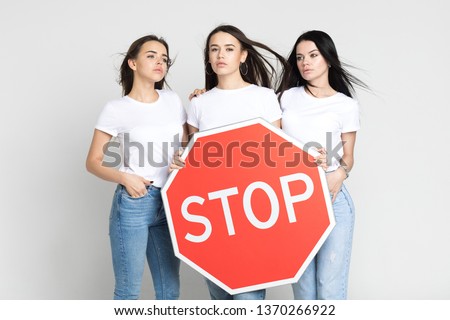 Three beautiful young women hold a big red stop sign.